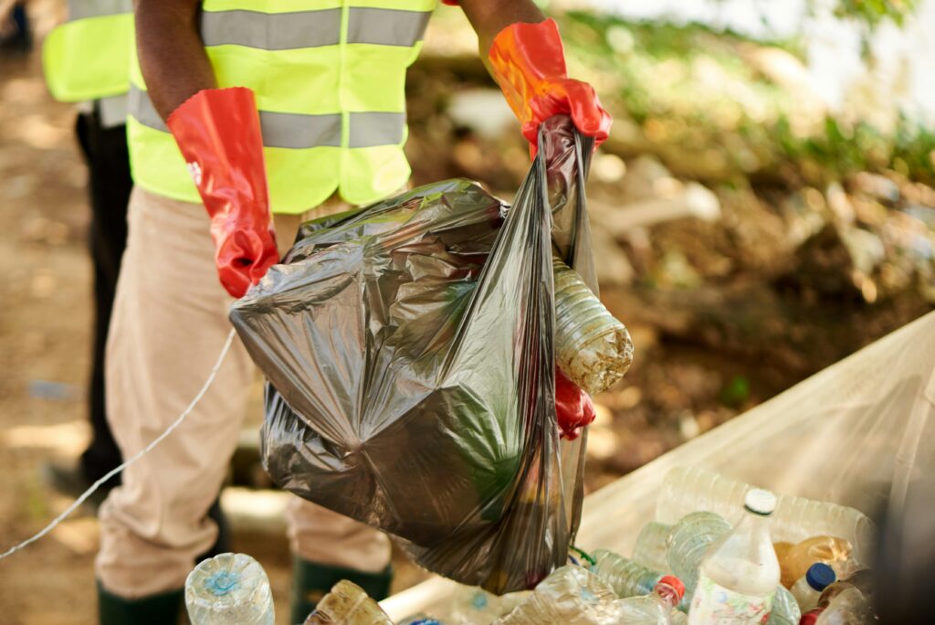 Person in gloves collecting plastic waste outdoors in Douala, Cameroon.