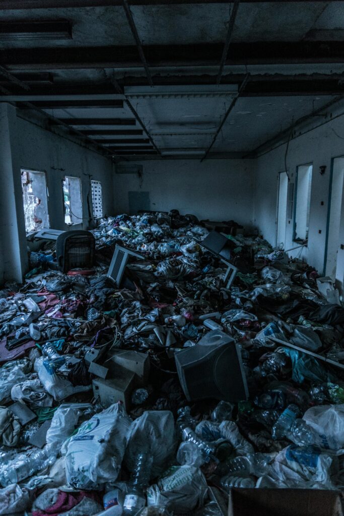 Decrepit indoor room cluttered with heaps of garbage and waste materials.